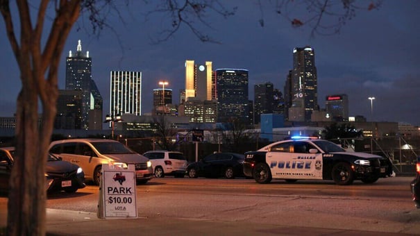 Dallas PD cars parked with their lights on and the Dallas skyline behind them 